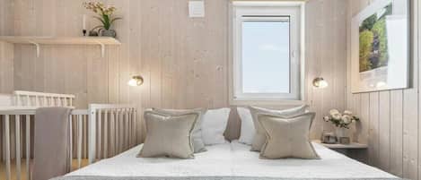 Un dormitorio con suelo de madera, una cama blanca con almohadas color beige, una ventana y un estante en la pared con flores.