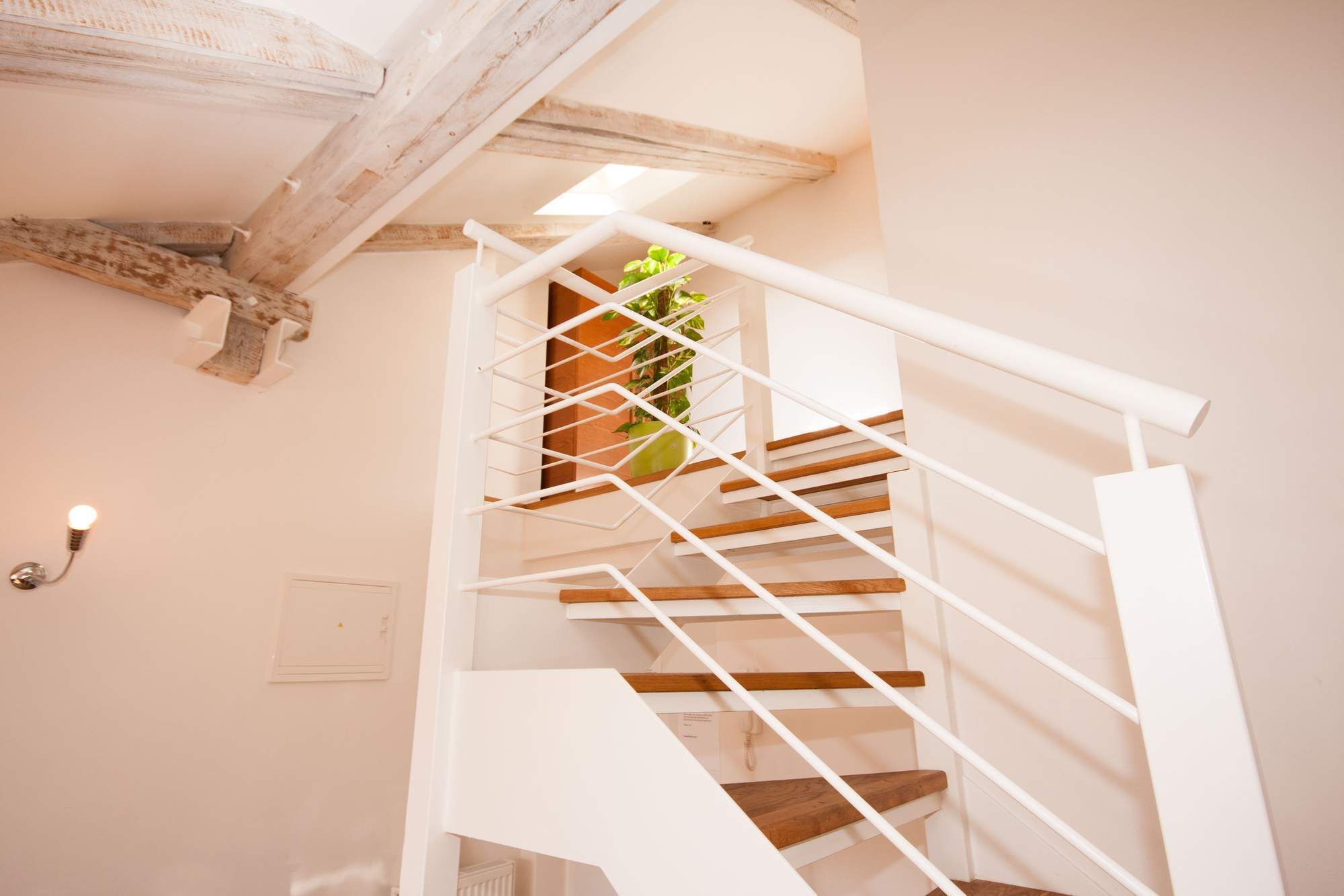 Un escalier en colimaçon blanc, avec des marches en bois et une rampe en métal, menant à l’étage supérieur.