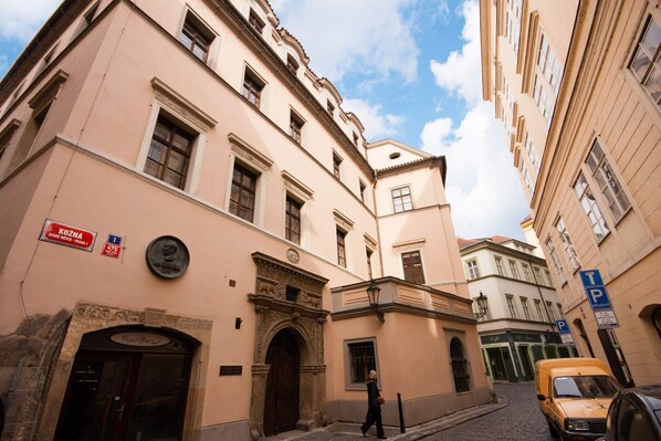 A narrow street with buildings featuring classical architecture, a visible entrance with an ornate archway, and a yellow taxi parked on the side. - Spacious Kozna Loft D 2-Bedrooms apartment in Prague Old Town (Prague)