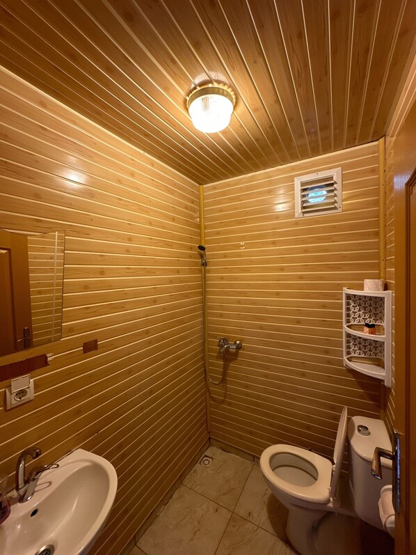 A small, compact bathroom with wooden paneling, a sink, toilet, and a shower. - Natural Pansiyon (Kumluca)