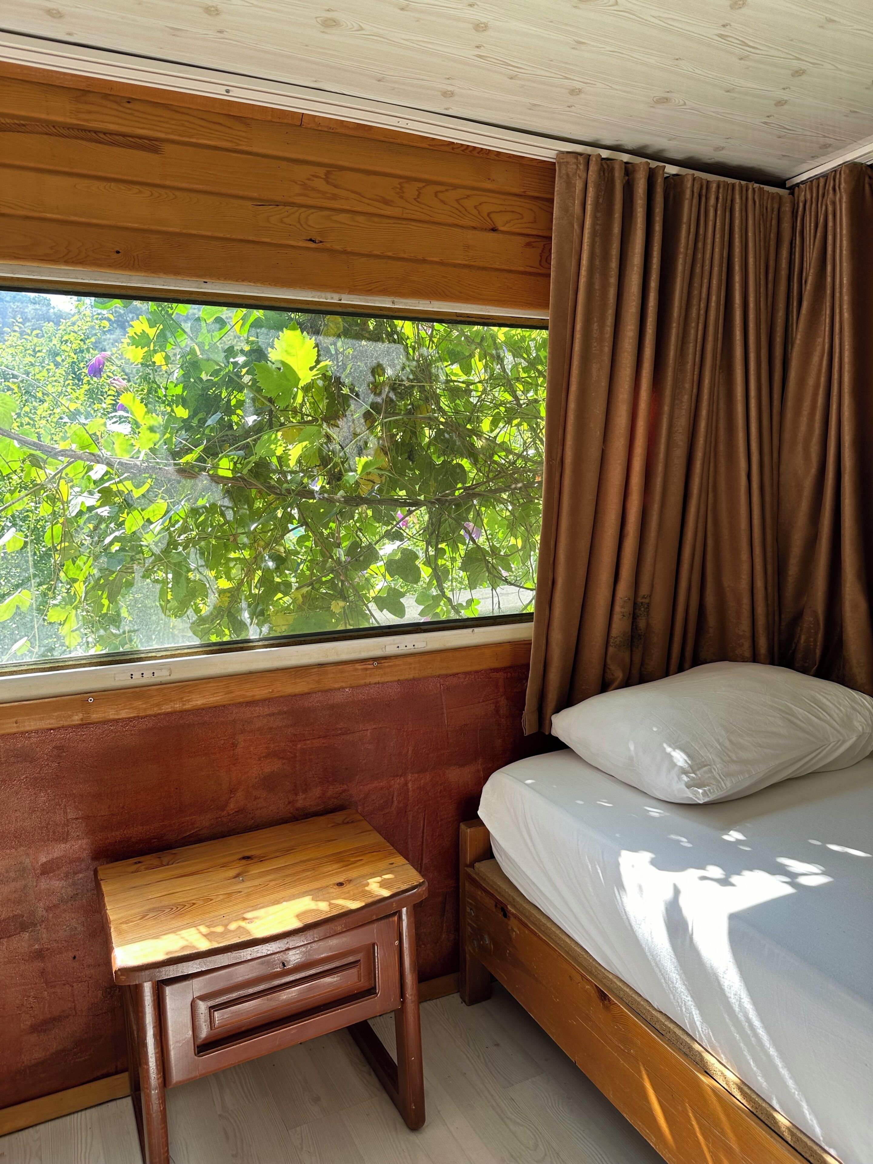 Une pièce avec un lit, une petite table en bois et une fenêtre avec des rideaux.