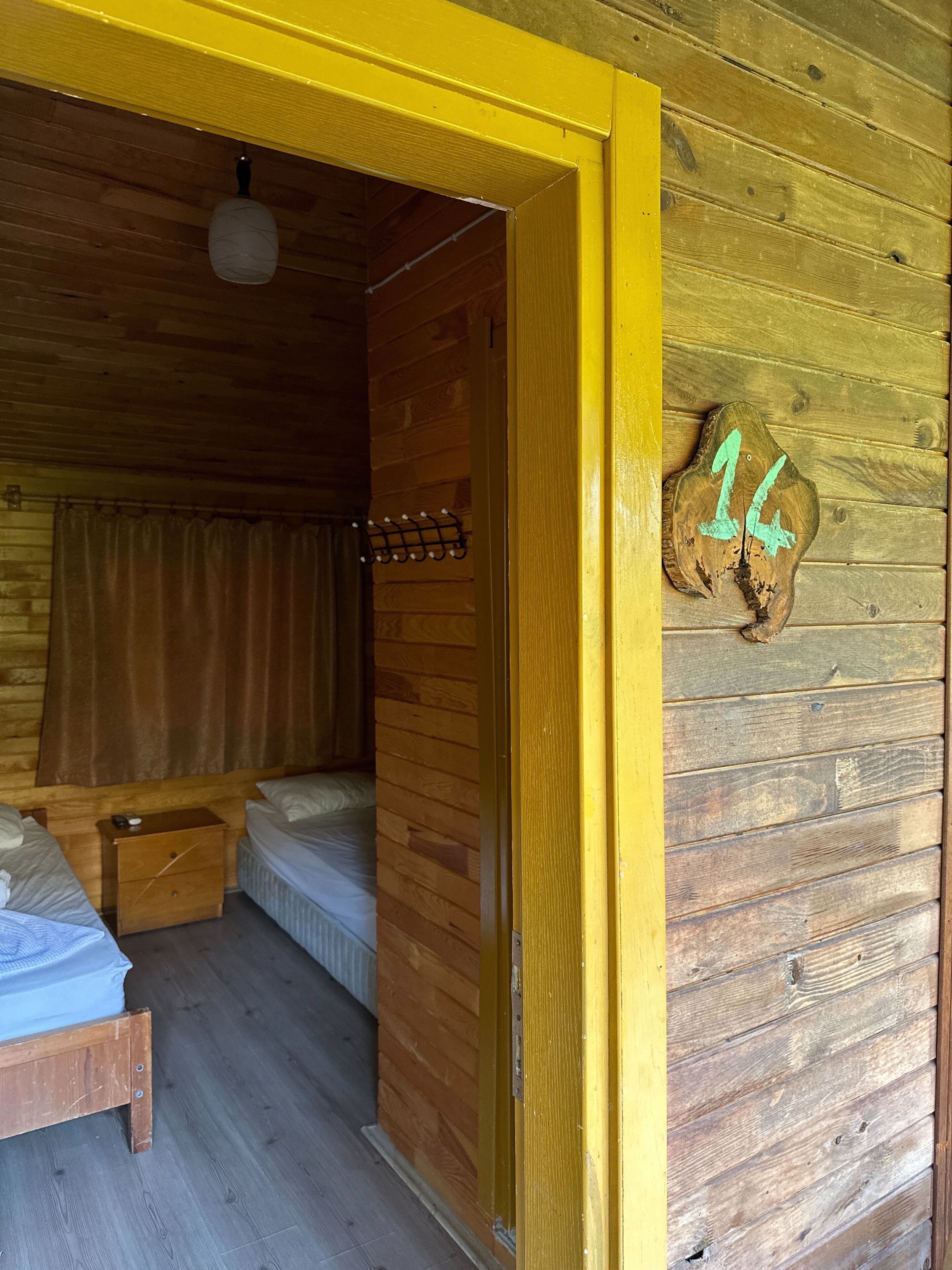 Interior de una cabaña de madera con una cama, una mesita y un perchero en la pared.