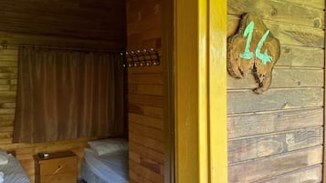 Interior de una cabaña de madera con una cama, una mesita y un perchero en la pared.