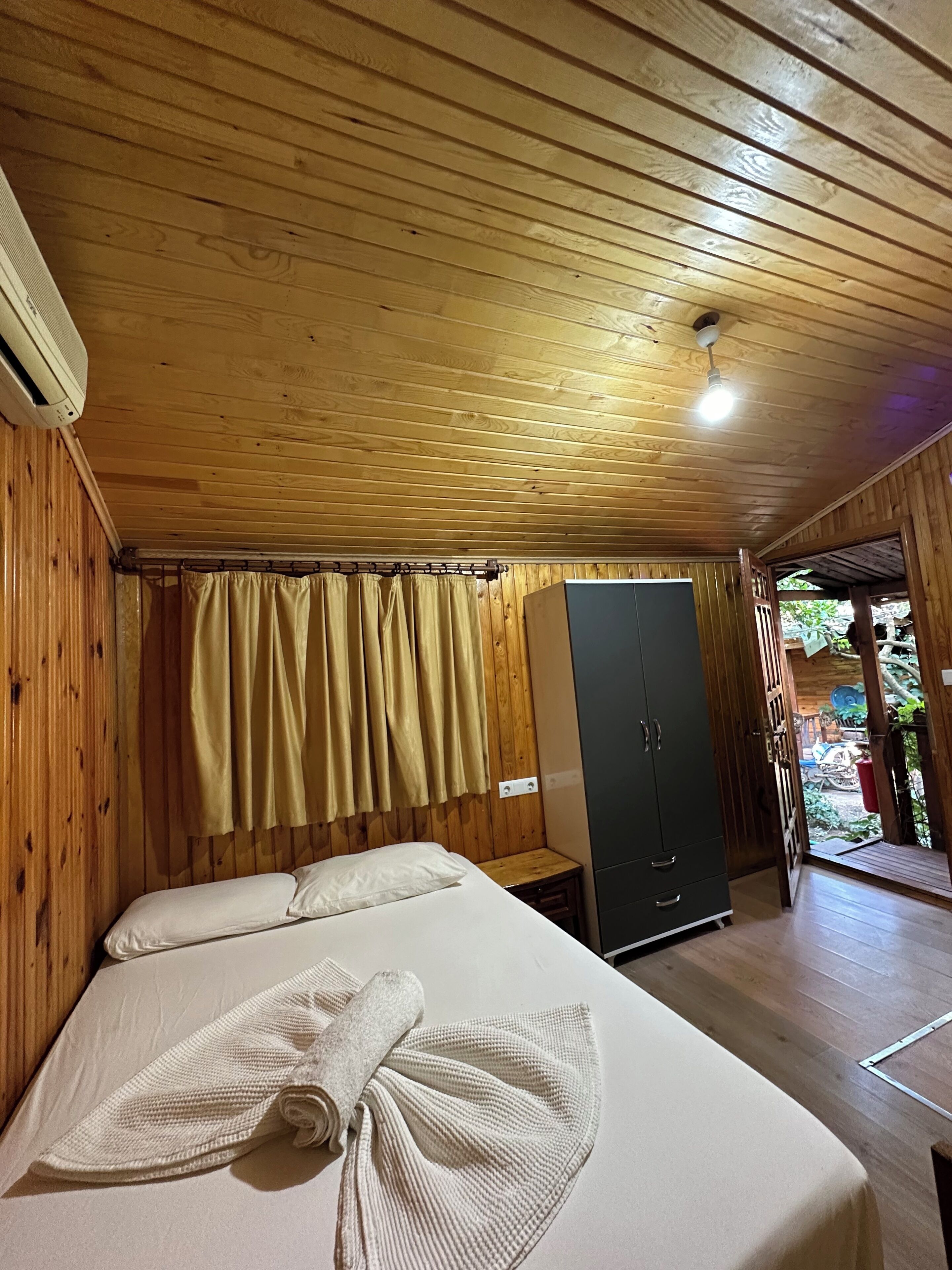 A wooden cabin room with a bed, a wardrobe, and a curtain.