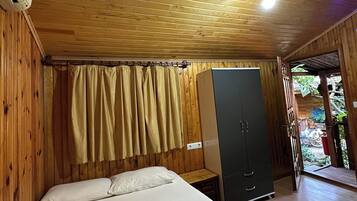 A wooden cabin room with a bed, a wardrobe, and a curtain.