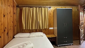 A room with wooden walls and ceiling, a bed with white linens, a wardrobe, and a ceiling fan.
