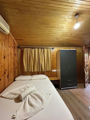 A room with wooden walls and ceiling, a bed with white linens, a wardrobe, and a ceiling fan.
