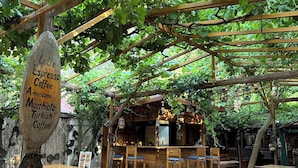 An outdoor café with wooden tables and benches, a sign indicating coffee types, and a rustic wooden structure in the background. - Natural Pansiyon (KUMLUCA)
