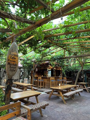 Un café a l'aire lliure amb taules i bancs de fusta, un cartell que indica tipus de cafè i una construcció de fusta rústica al fons.