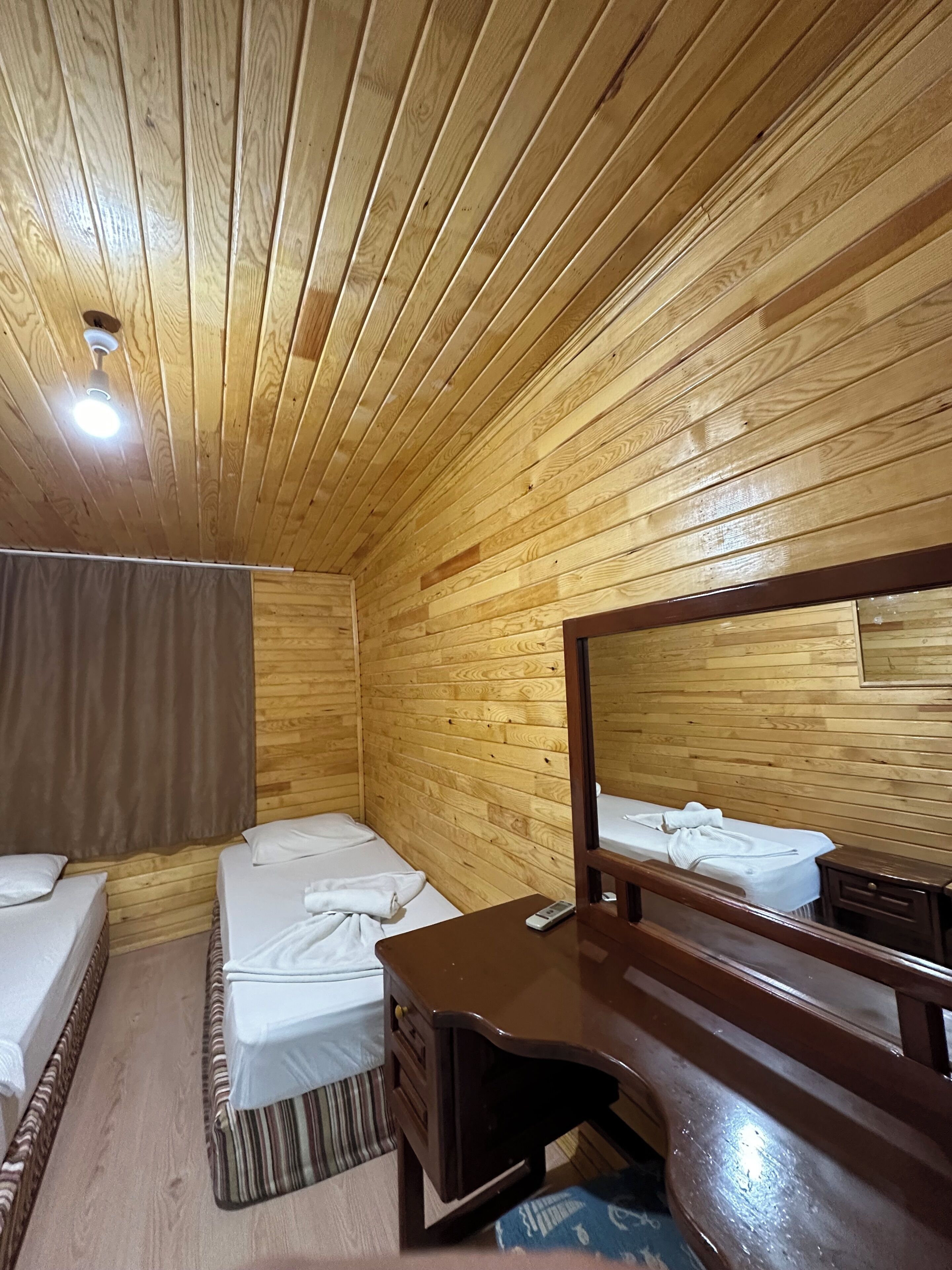 A wooden-paneled room with two beds, a desk, and a mirror.