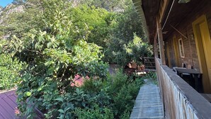 A wooden building with a covered outdoor area, a staircase leading to a mountain view, and a red-roofed structure in the background.