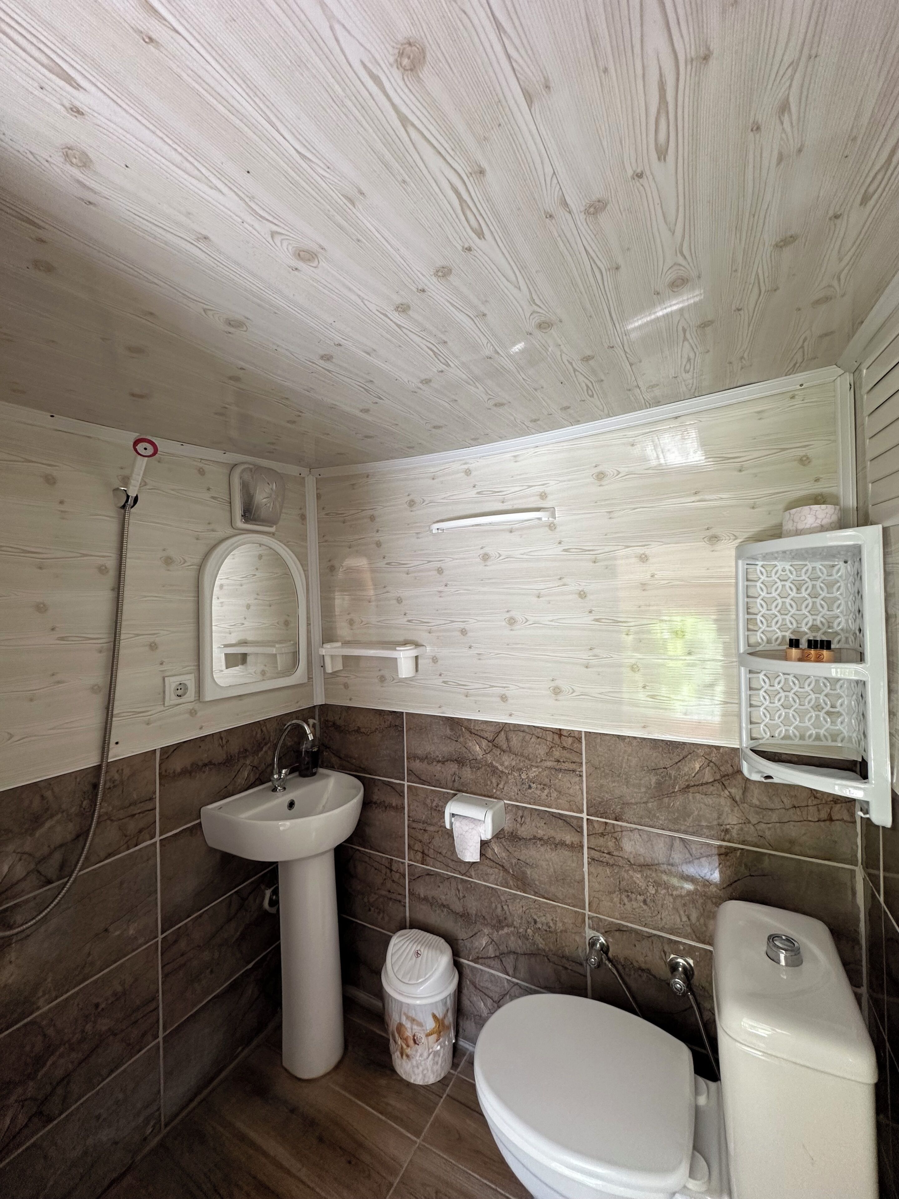 Et badeværelse med træloft, vask, toilet og brusebad.