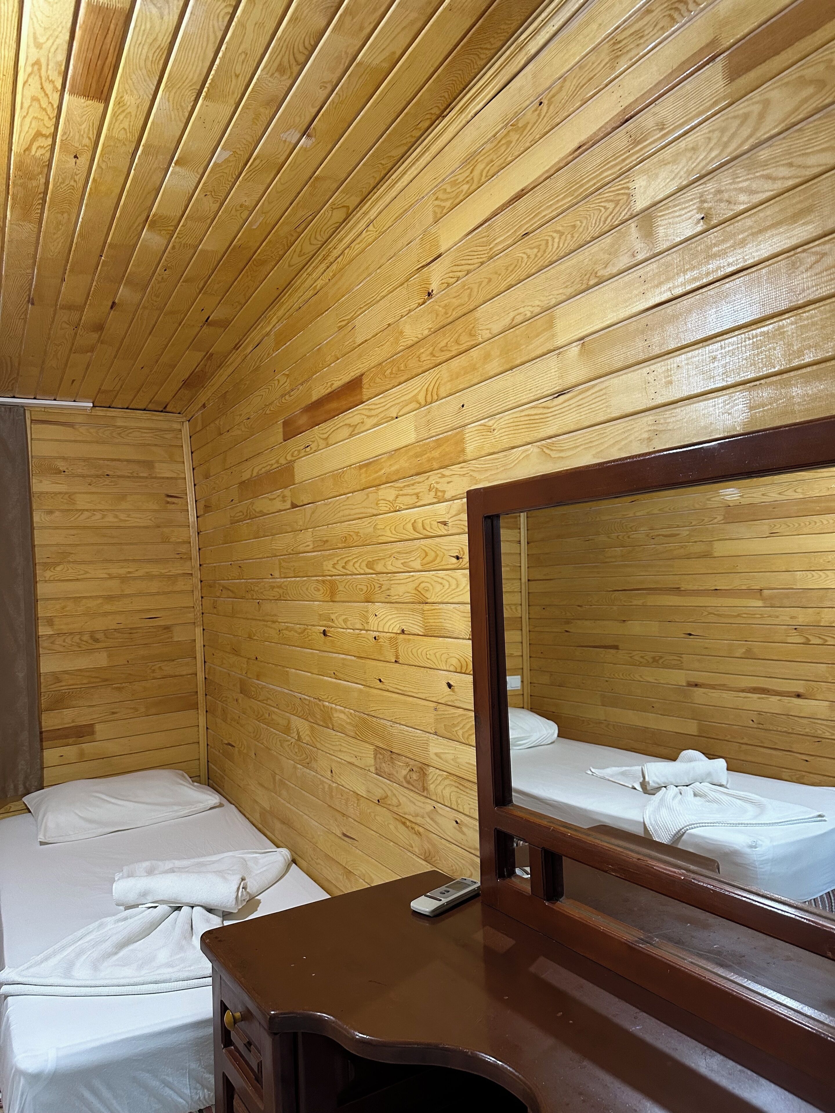 A wooden-paneled room with two beds, a mirror, and a wooden dresser.