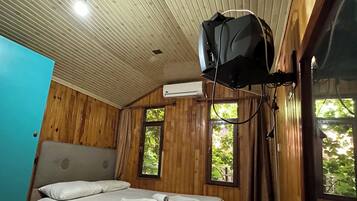 A room with a bed, wooden walls, a ceiling fan, an air conditioning unit, and windows with natural light.