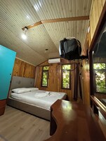 Habitación con cama, paredes de madera, ventilador de techo, equipo de aire acondicionado y ventanas con luz natural.