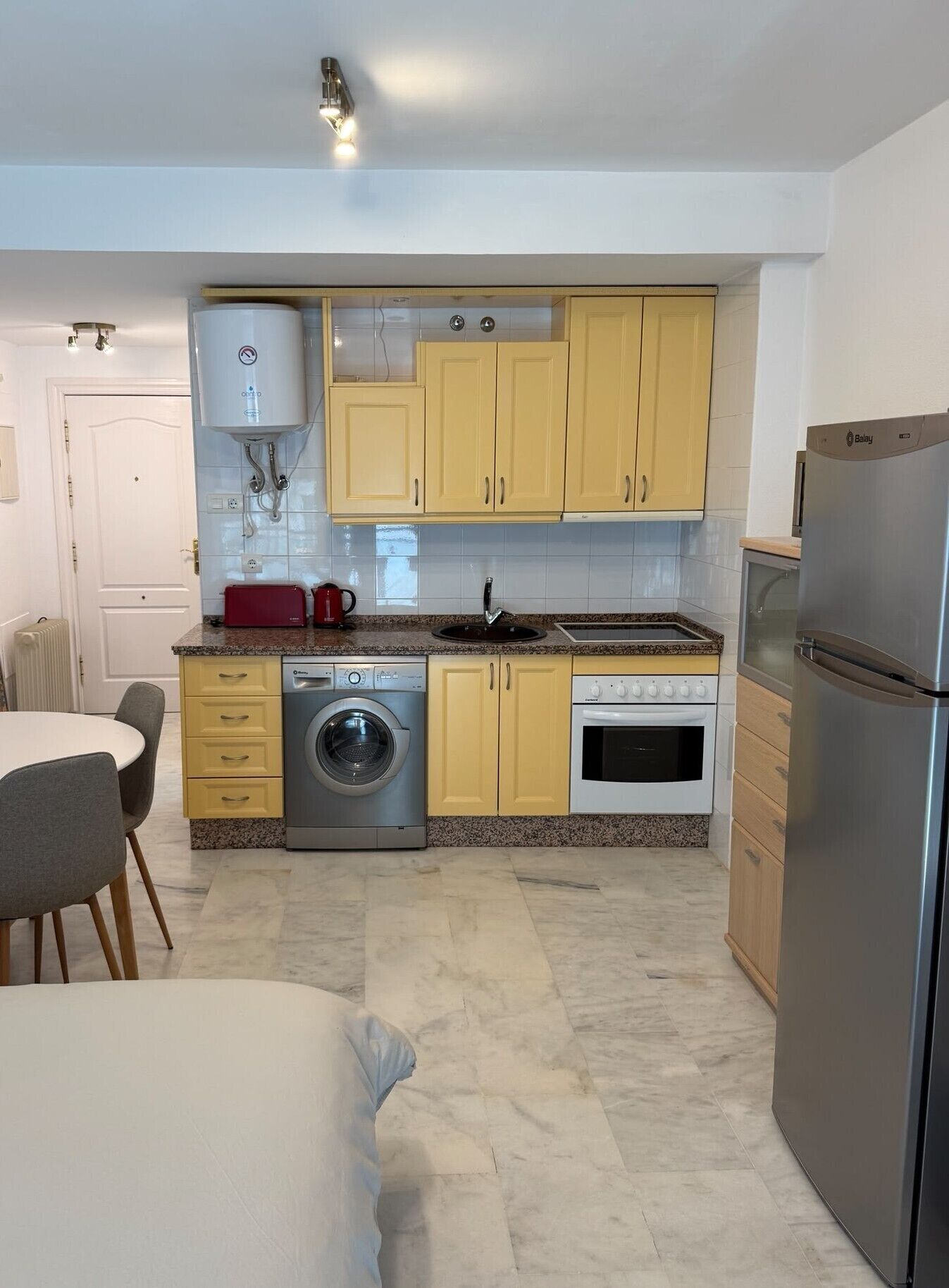 A compact kitchen with a washing machine, oven, and a refrigerator.