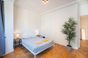 Een slaapkamer met een bed, bedlampen, een potplant en een houten vloer.