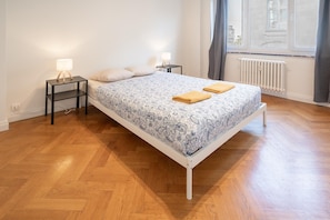 A bedroom with a bed, two bedside tables, a window with curtains, and a radiator. - 3-bedroom family apartment (Antwerp)