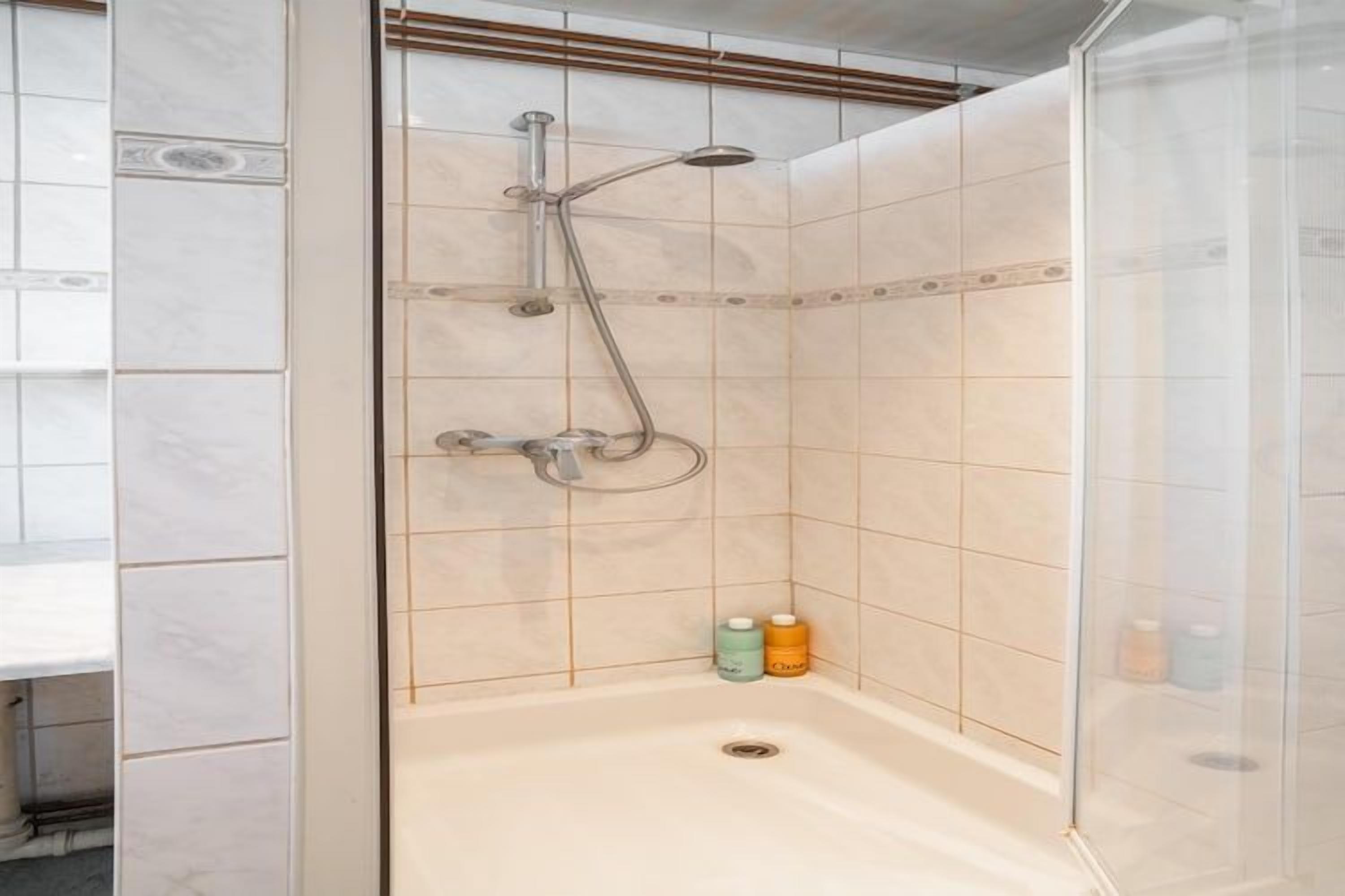 A shower with a glass enclosure, a handheld showerhead, and two bottles of shampoo on the floor.