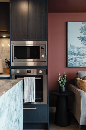 A modern kitchen with a built-in microwave and oven, a marble countertop, and a potted plant on a side table. - The Southwest Pottery Suite | DT Kelowna 1BR | Pool&Sauna (Kelowna)