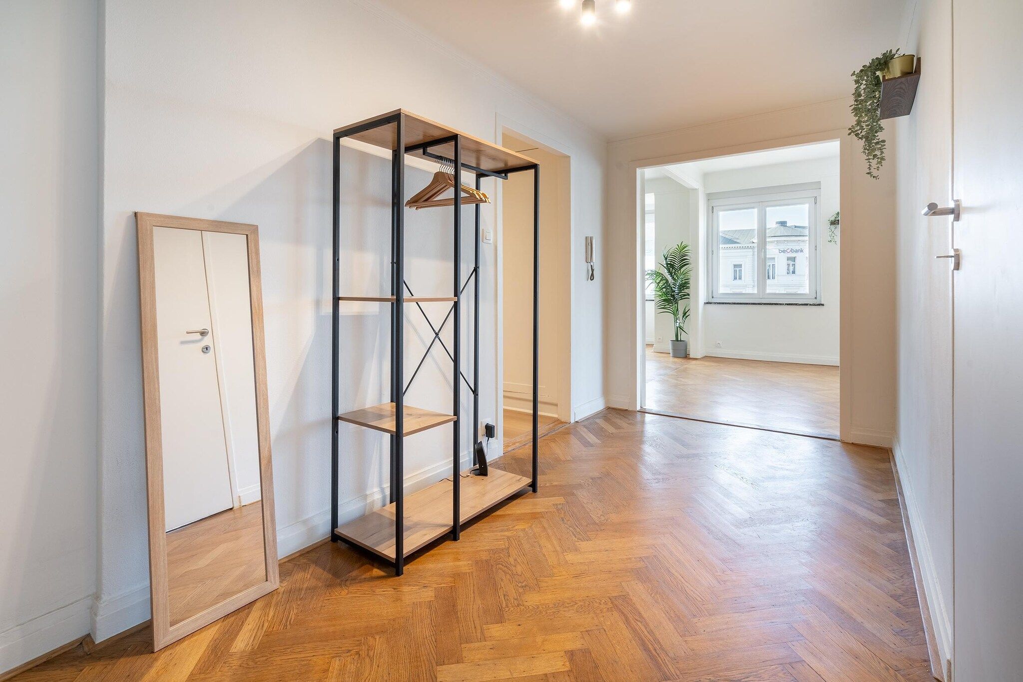 A hallway with a wooden floor, a wardrobe, and a metal shelving unit with a coat rack.