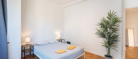 A bedroom with a bed, bedside lamps, a potted plant, and a wooden floor.