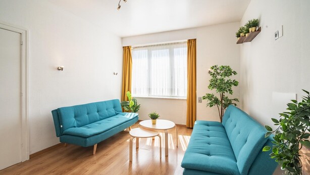 Una sala de estar con dos sofás azules, una mesita redonda y una ventana con cortinas.