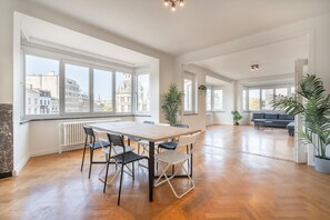 A spacious living area with a large table and chairs, a sofa, and several potted plants. - Spacious 3-Bedroom Apartment (Antwerp)