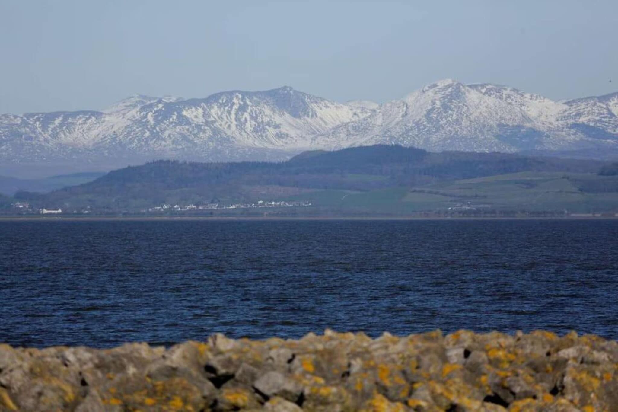 Eine Küstenlandschaft mit schneebedeckten Bergen im Hintergrund und einer felsigen Uferlinie im Vordergrund.