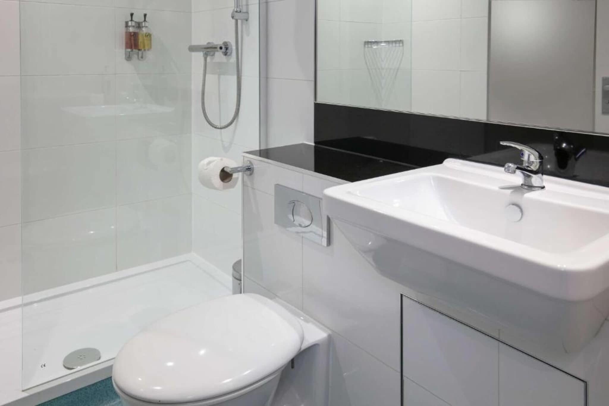 Un baño moderno con inodoro blanco, lavamanos blanco y zona de ducha.