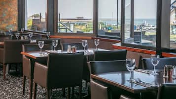 A restaurant with tables and chairs, large windows with a view of the cityscape.