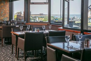 Un restaurant avec des tables et des chaises, de grandes fenêtres offrant une vue sur le paysage urbain.