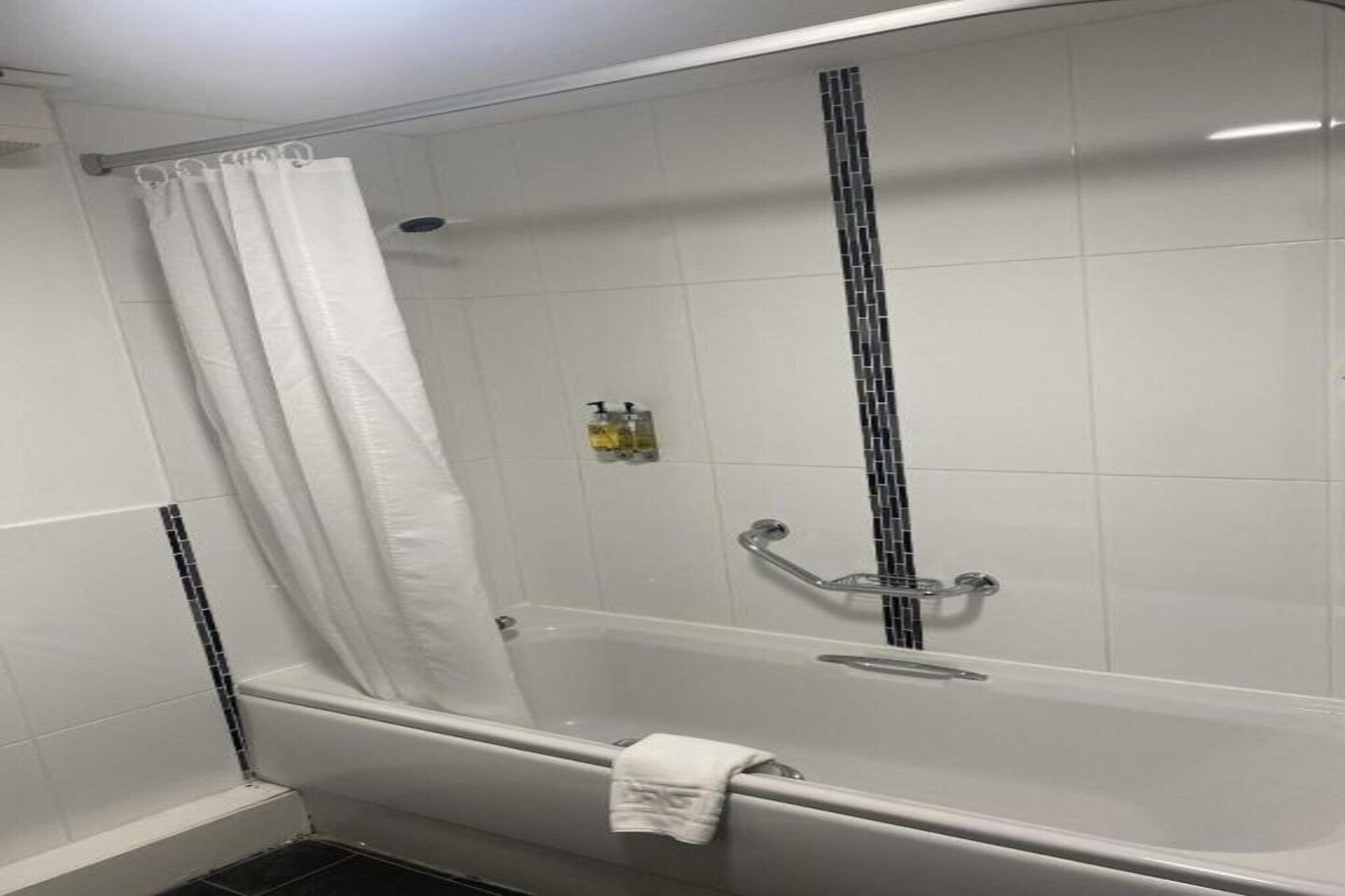 A white tiled shower enclosure with a glass door, a showerhead, and a handheld shower attachment.