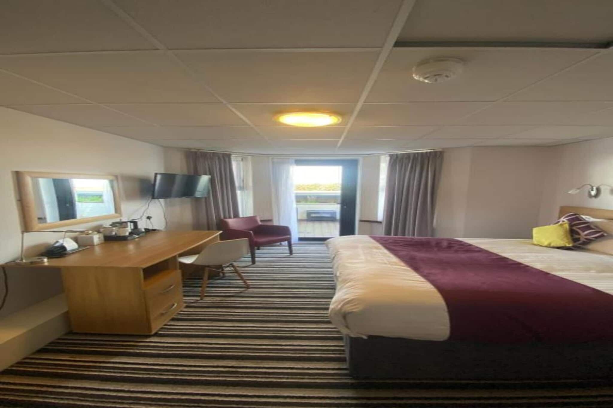 A hotel room with a bed, a desk, a chair, a television, and a window.
