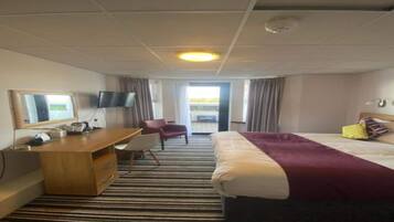 A hotel room with a bed, a desk, a chair, a television, and a window.