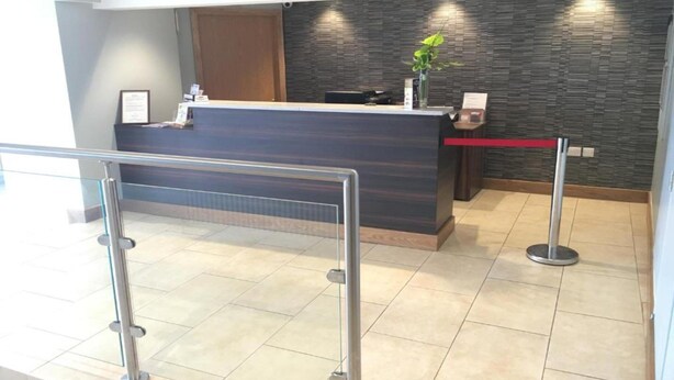 A reception desk with a modern design, a plant on the counter, and a red barrier in front. - Standard Double Room (Lancaster)