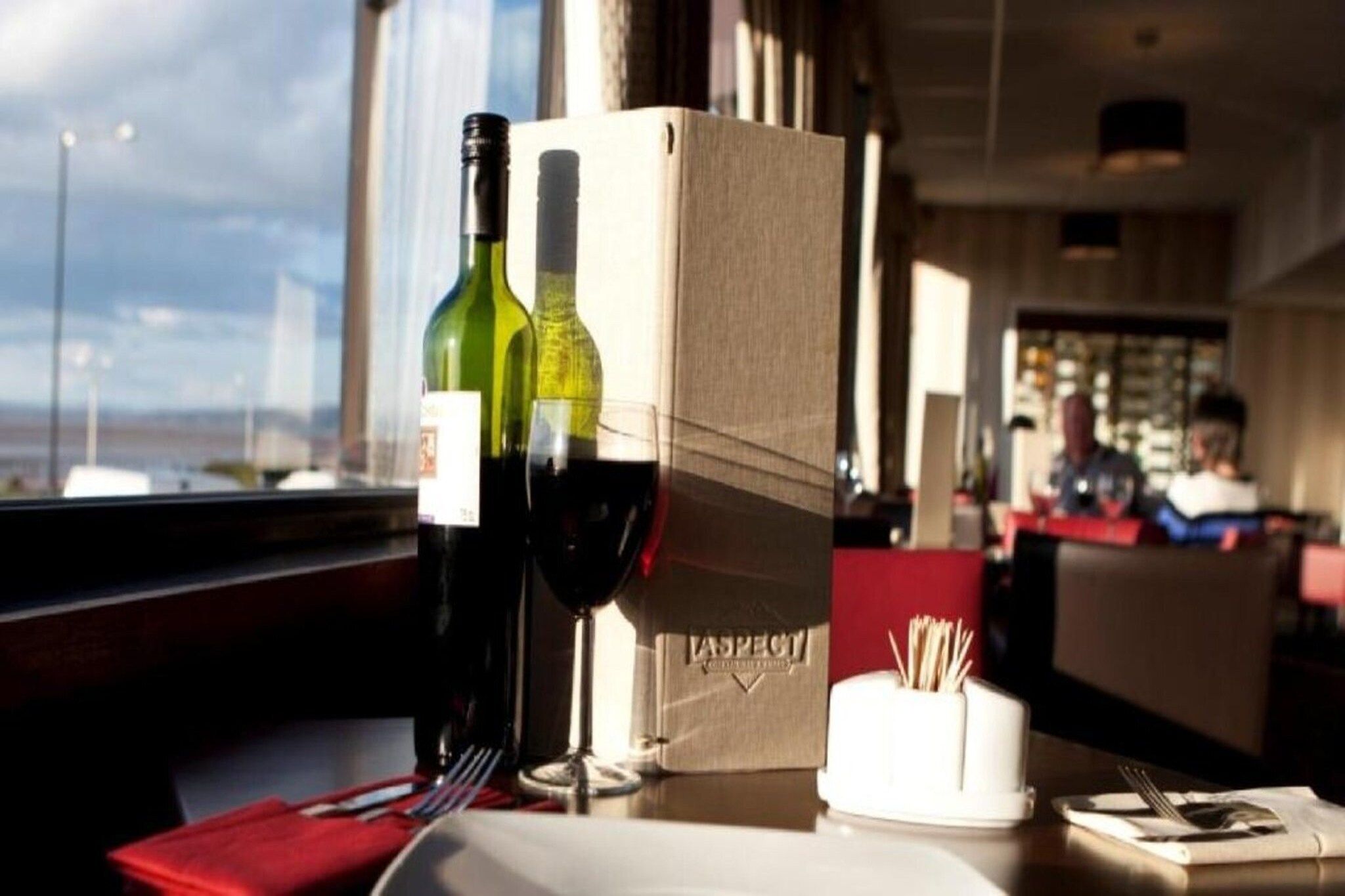 A restaurant setting with a table set for two, a wine bottle, and a menu box.