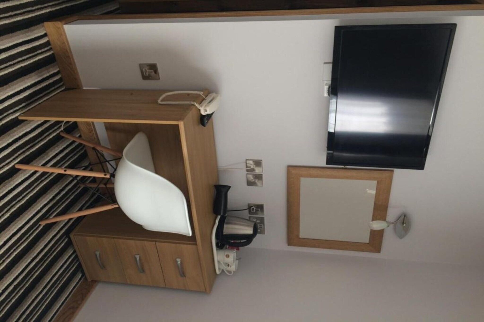 Een verzorgde, kleine kamer met een houten bureau, een witte stoel, een flatscreen televisie en een klein kastje.