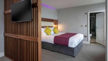 A hotel room with a bed, a television mounted on a wooden panel, and a bathroom visible through an open door.