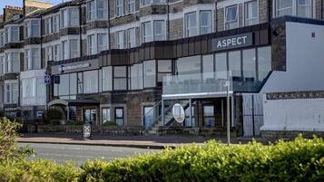 A hotel named ASPECT with a modern facade, a visible entrance, and a sign indicating a nearby parking area.