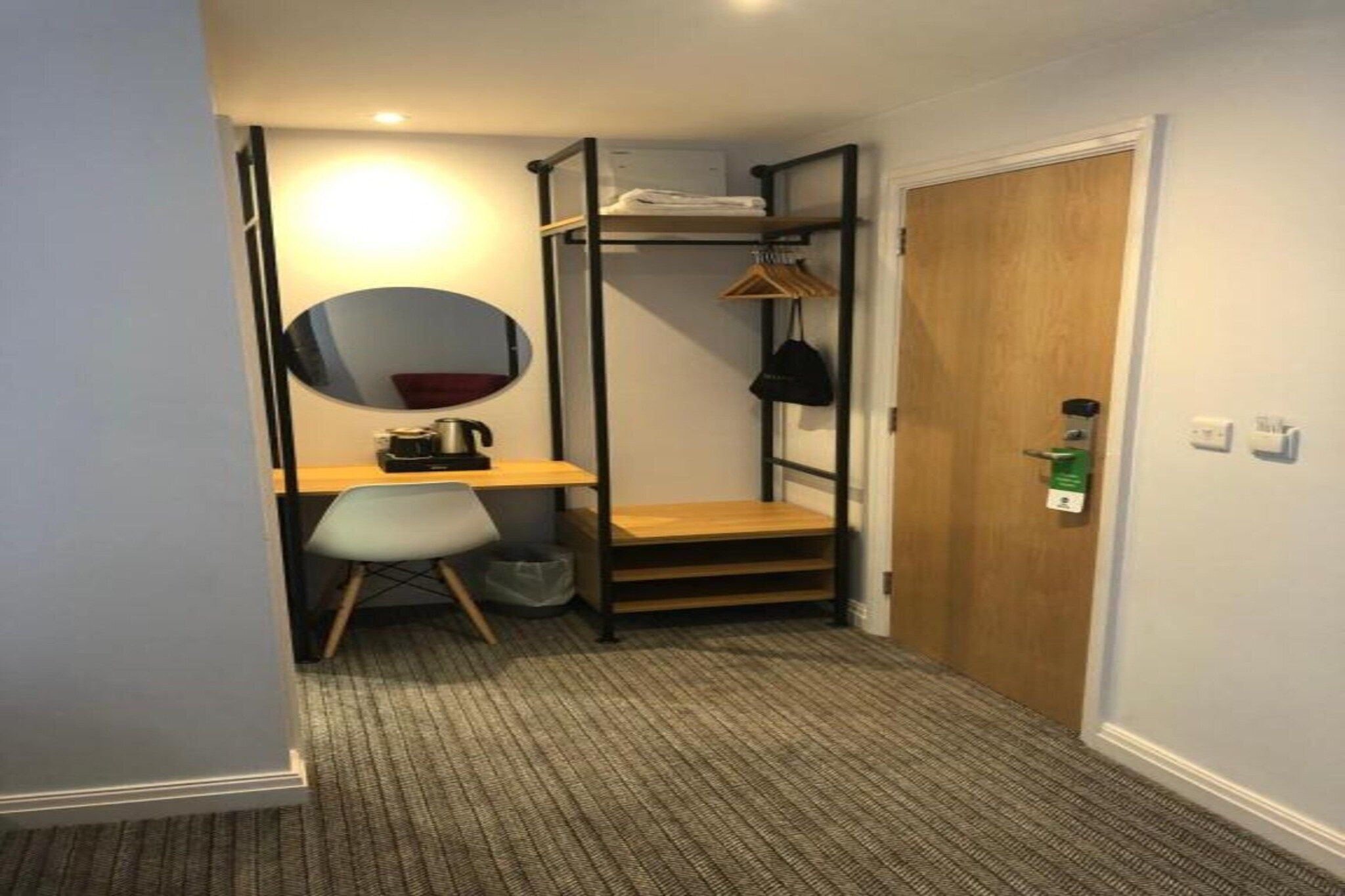 A compact room with a bunk bed, a desk, a chair, a mirror, and a door.