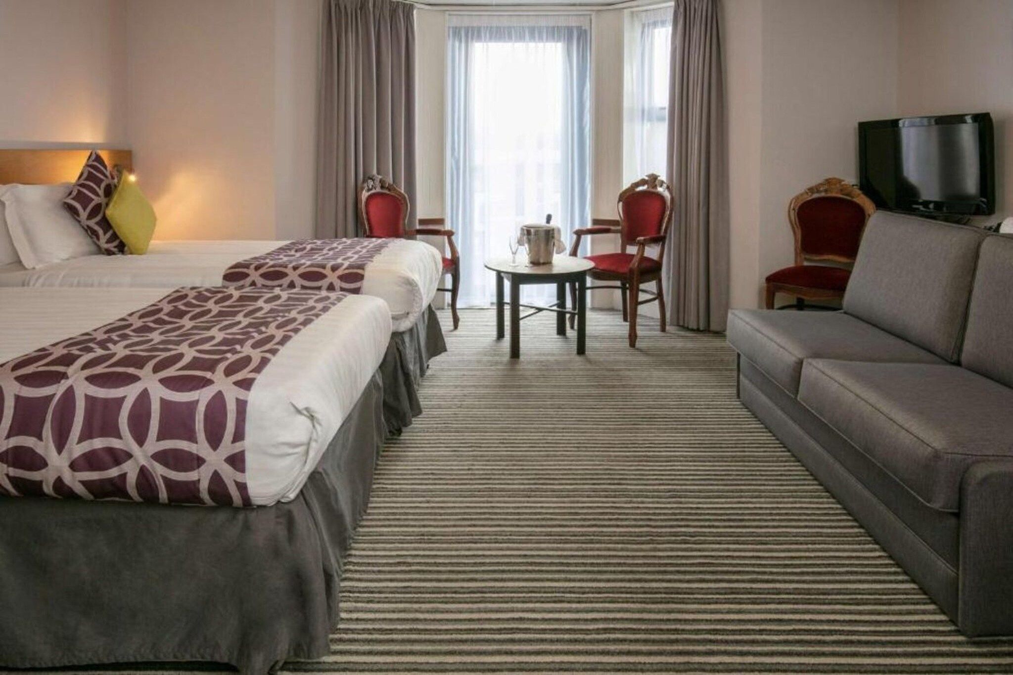 A hotel room with two beds, a sofa, a TV, and a dining area with chairs and a table.