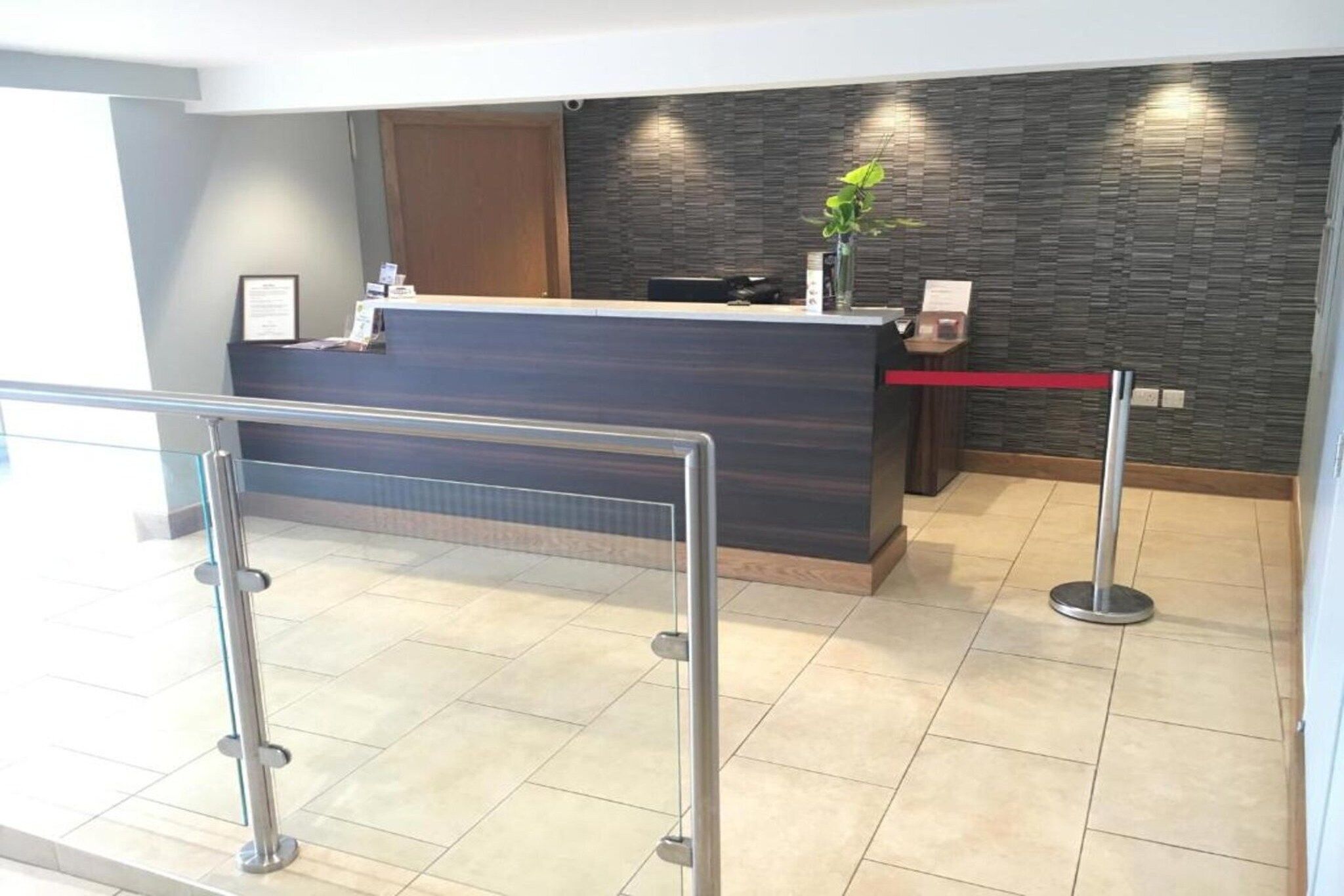 A reception desk with a modern design, a plant on the counter, and a red barrier in front.