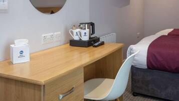 A hotel room with a wooden desk, a chair, a bed with a red blanket, a coffee maker, and a tissue box.