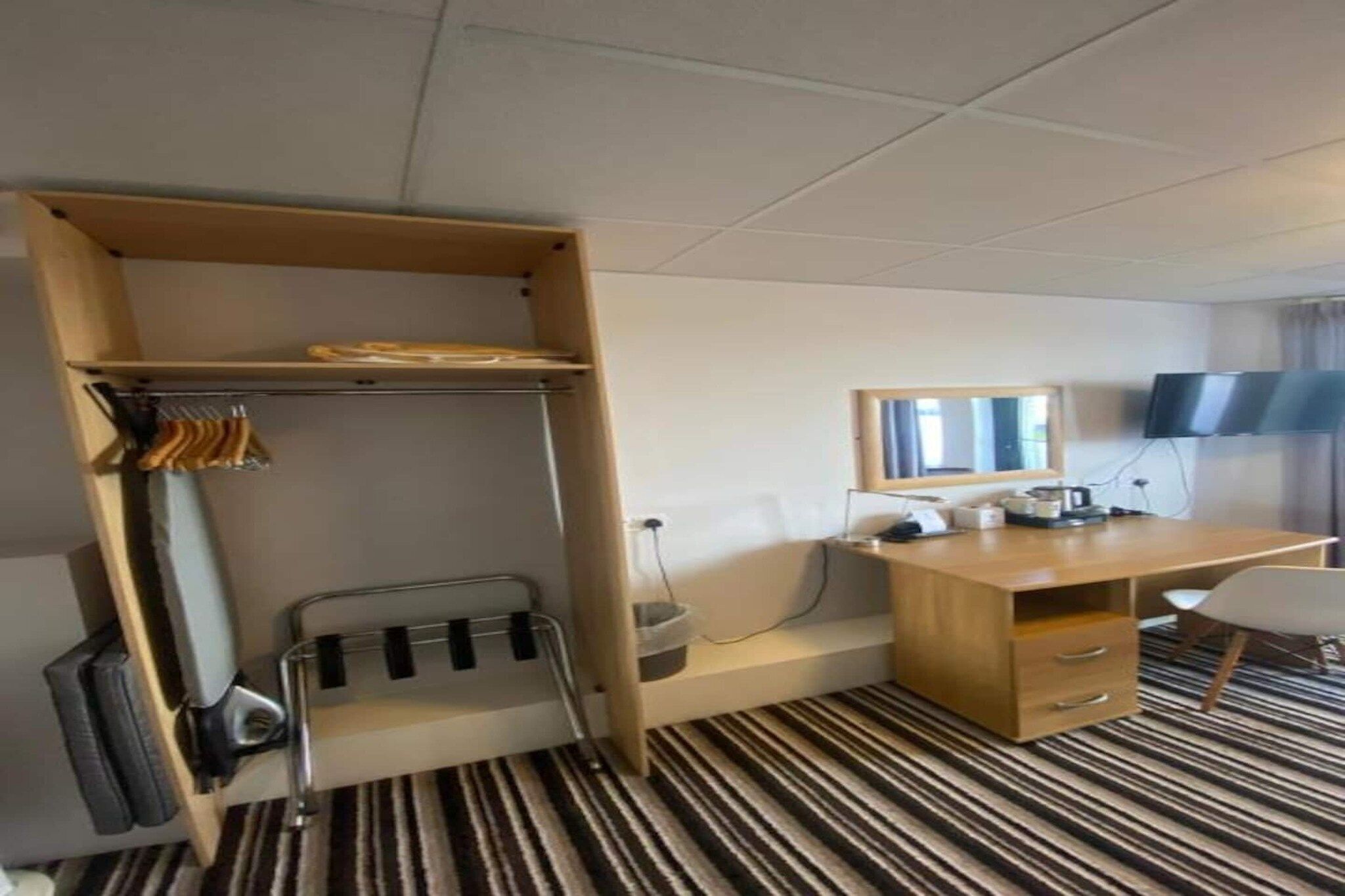 A hotel room with a bunk bed, a desk, a chair, a flat-screen TV, and a striped carpet.