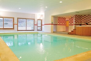 An indoor swimming pool with clear water, a checkered wall, and a wooden bench area. - Stylish Studio for 2 in Auvergne (Brides-les-Bains)