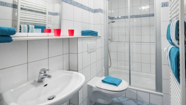 A bathroom with a white sink, a toilet, a shower, and a towel rack with blue towels. - Haus Schmalenbeck JBH 1 (Norderney)