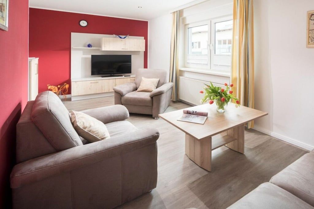 Ein Wohnzimmer mit einer Couch, einem Couchtisch, einem Fernseher und einem Fenster mit Vorhängen.