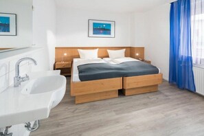 Ett modernt hotellrum med en säng i trä, ett vitt handfat och ett nattduksbord.
