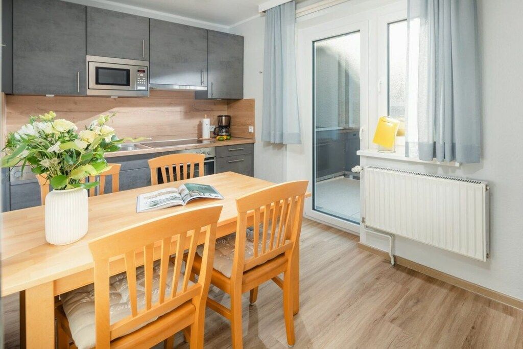 Eine moderne Küche mit grauen Schränken, einer Mikrowelle und einem Essbereich mit einem Holztisch und Stühlen.